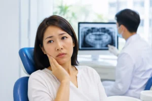 Patient experiencing lower jaw discomfort while a dentist reviews a panoramic dental X-ray